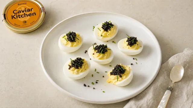 Deviled eggs topped with Baerii caviar and chives on a white ceramic plate