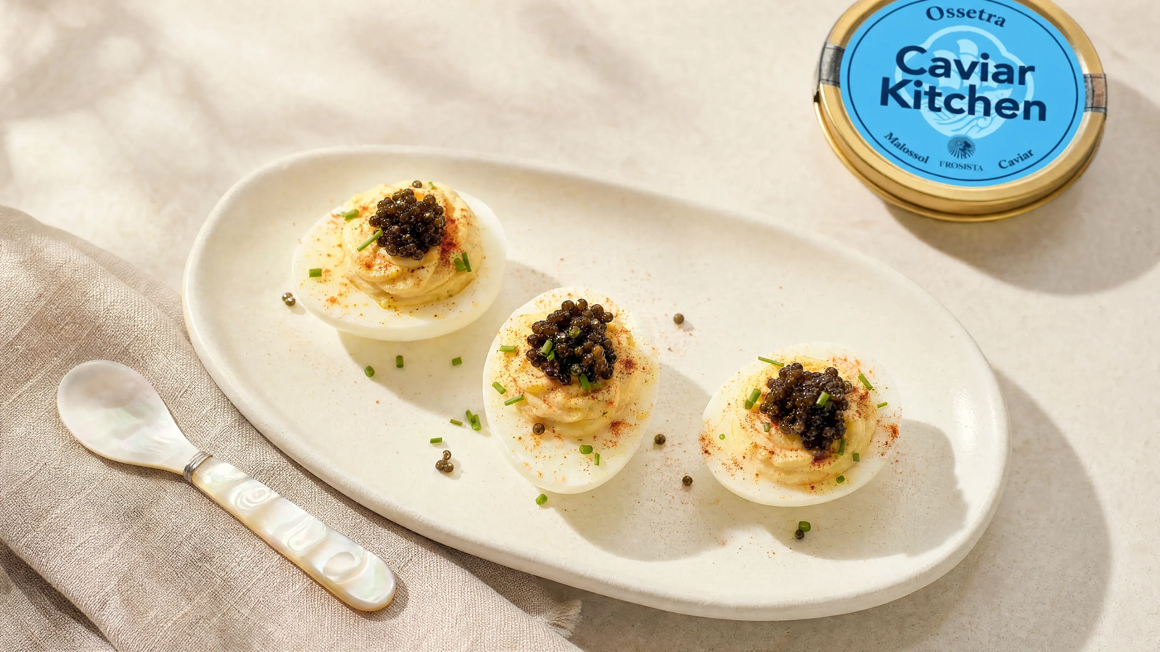 Three deviled eggs topped with Ossetra caviar and chives on a small white plate