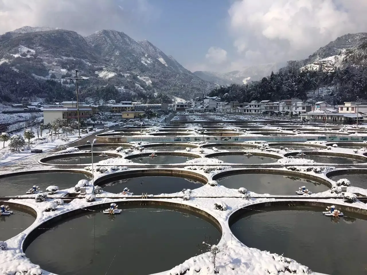 The same circular tanks under winter snow, with snow-covered mountains behind.