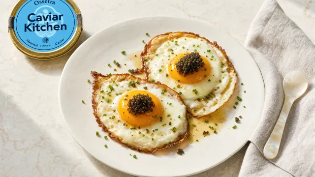 Two fried eggs with crispy edges topped with Ossetra caviar and chives on a white plate with a small spoon resting alongside
