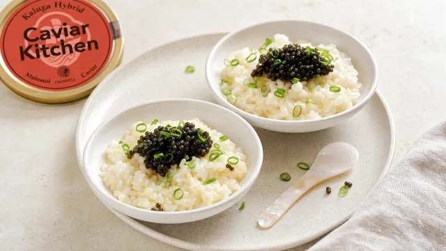 Two white bowls of buttered rice topped with Kaluga Hybrid caviar and sliced scallions on a light linen