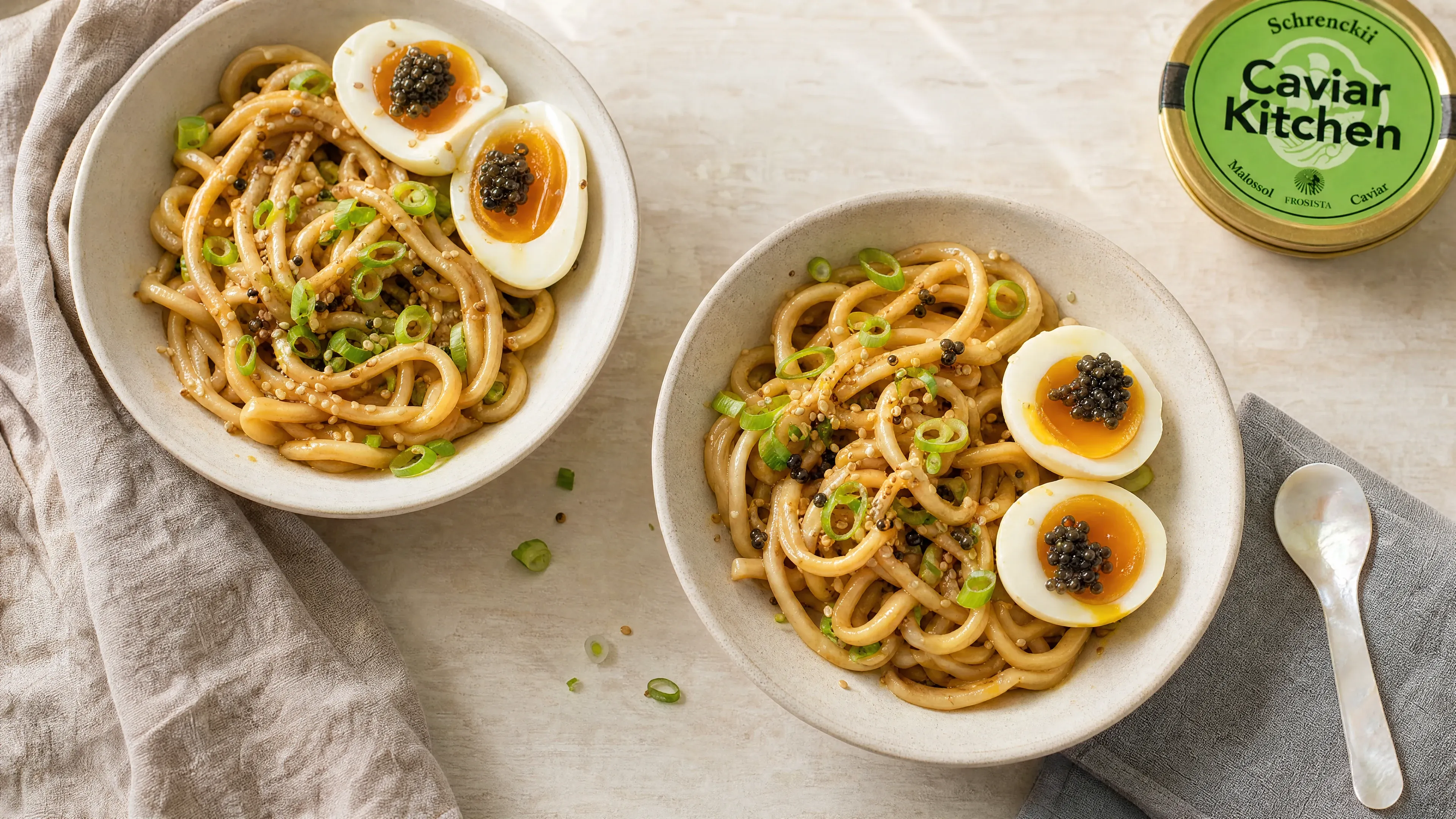 Two bowls of brown butter udon with halved jammy eggs topped with dark Schrenckii caviar and sliced scallions