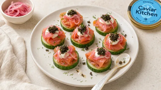 Cucumber rounds topped with smoked salmon, pickled red onion strands, crème fraîche, and Ossetra caviar on a white plate