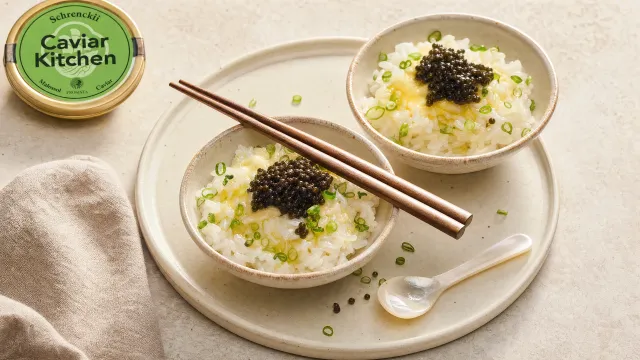 Two white bowls of steamed rice with melted butter, green onion, and a spoonful of dark Schrenckii caviar on top