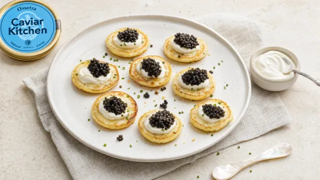 Potato blinis topped with crème fraîche and Ossetra caviar on a white ceramic plate, close up